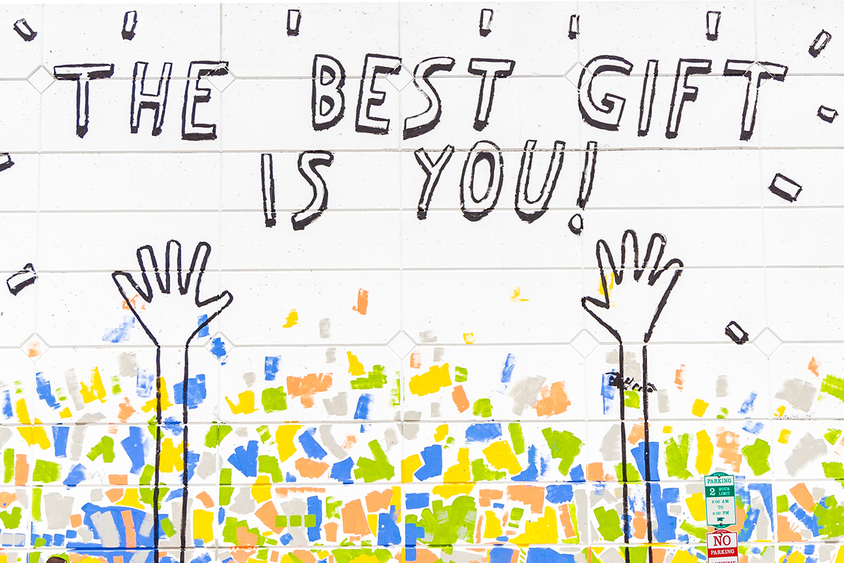 Image of a building wall with The Best Gift Is You painted on it